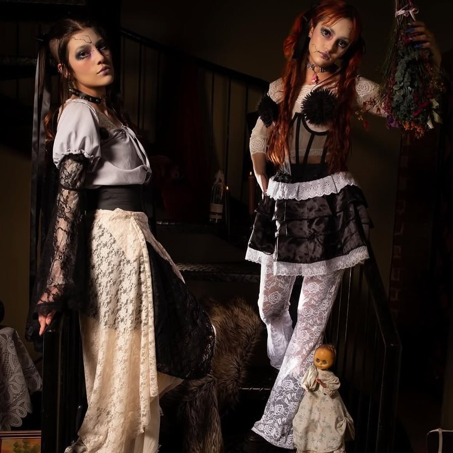 Dos modelos con estilismo de muñecas en encaje, satén negro y maquillaje de porcelana, en una escalera con flores secas