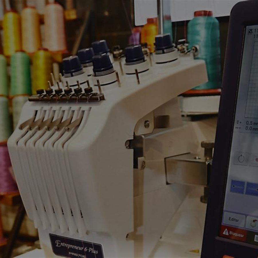Máquina de bordar con conos de hilo de colores y la pantalla de diseño del bordado