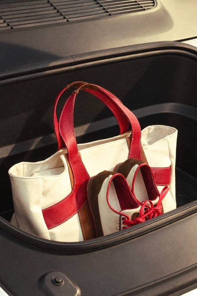 Bolso tote crema con asas rojas y zapatos crema y café dentro del baúl de un auto
