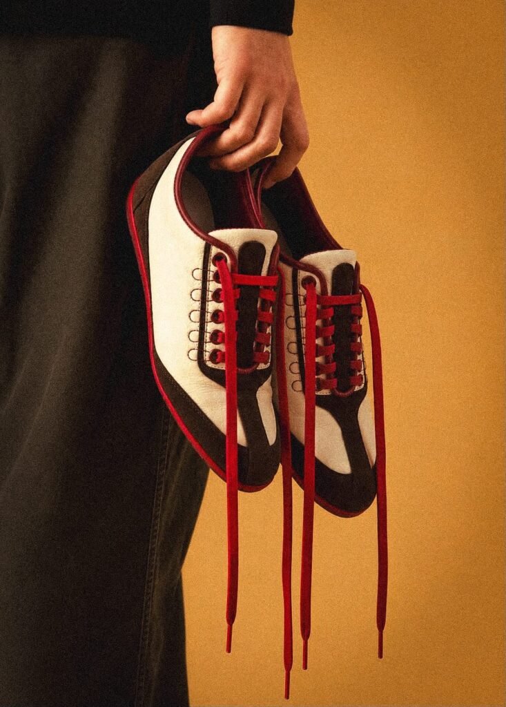 Zapatos de cuero blanco y gamuza café con cordones rojos sostenidos en la mano