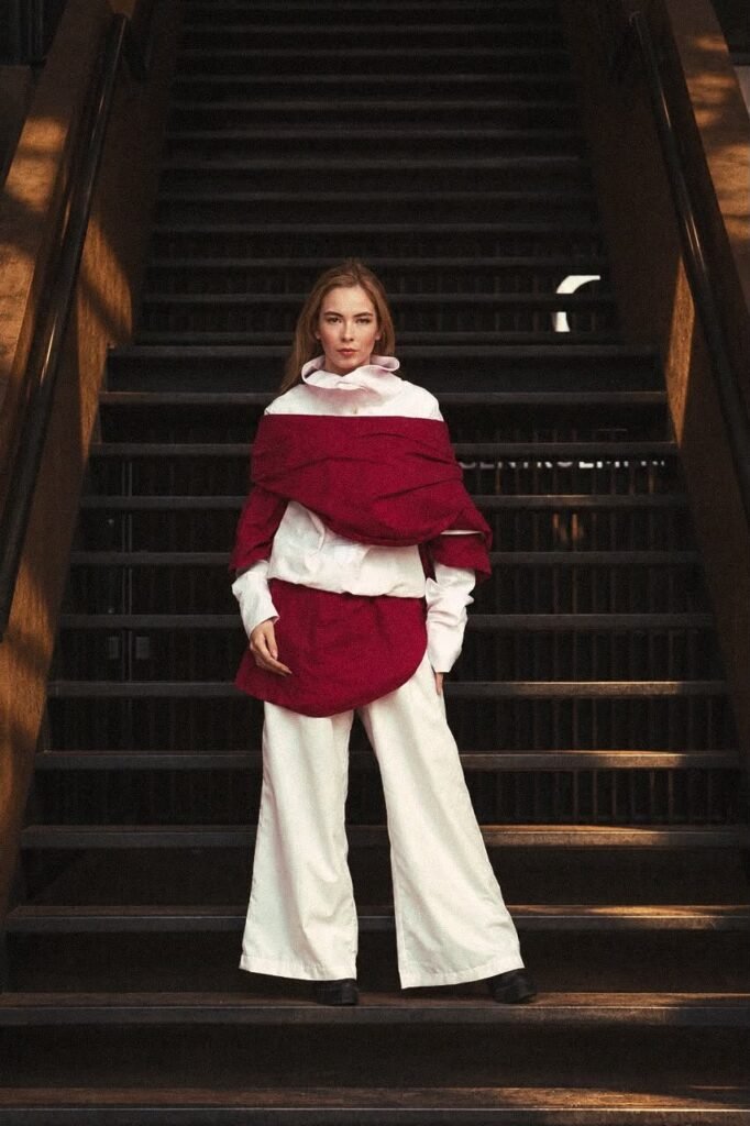 Modelo con capa roja envolvente, camisa rosa y pantalón ancho en una escalera